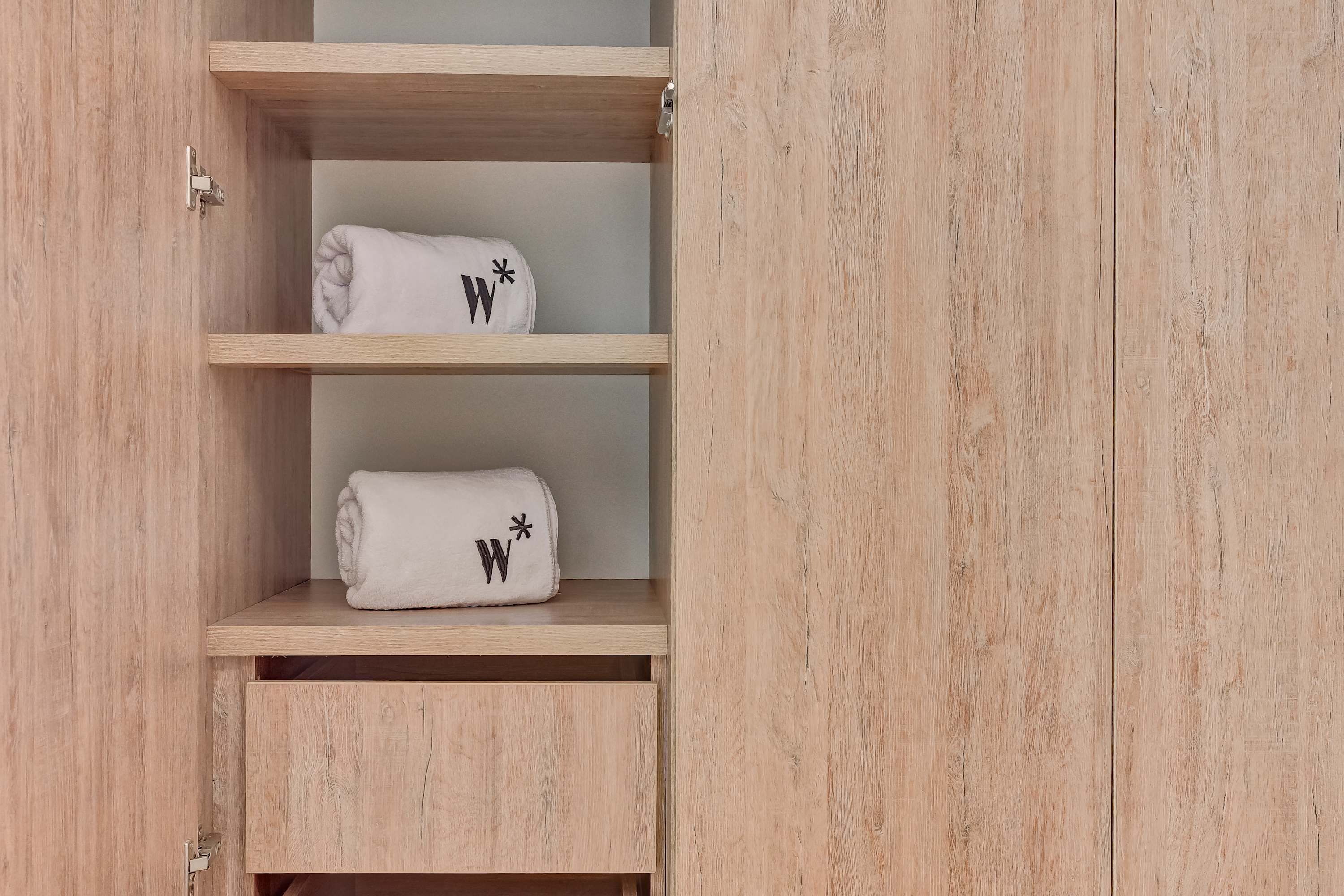 Un mueble de madera con dos estantes, cada uno con una toalla blanca enrollada y un símbolo negro.
