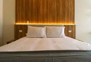 Een bed met een houten hoofdbord, twee kussens en een grijze deken.