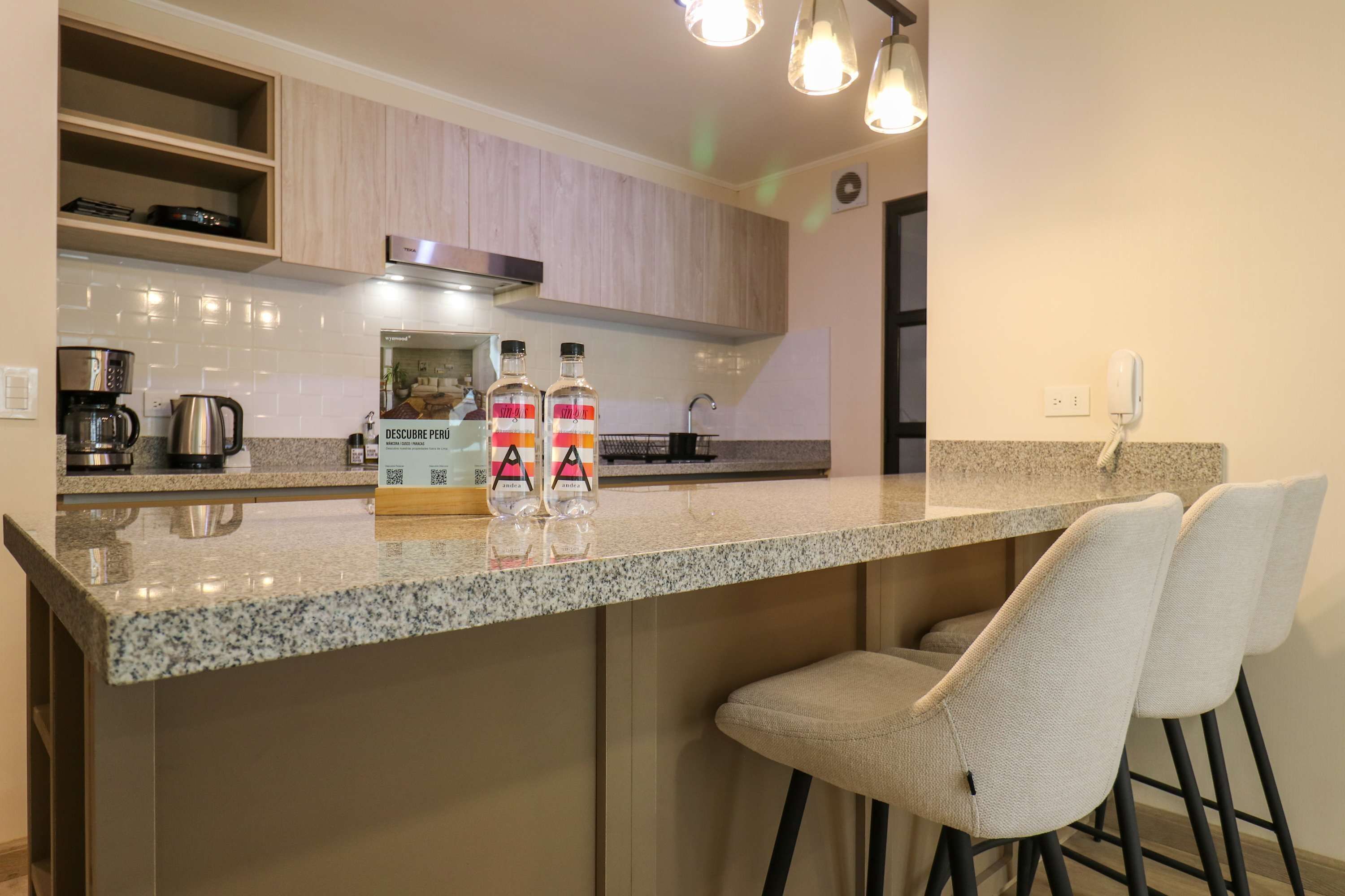 A kitchen with granite countertops, stainless steel appliances, and a bar area with two high stools.