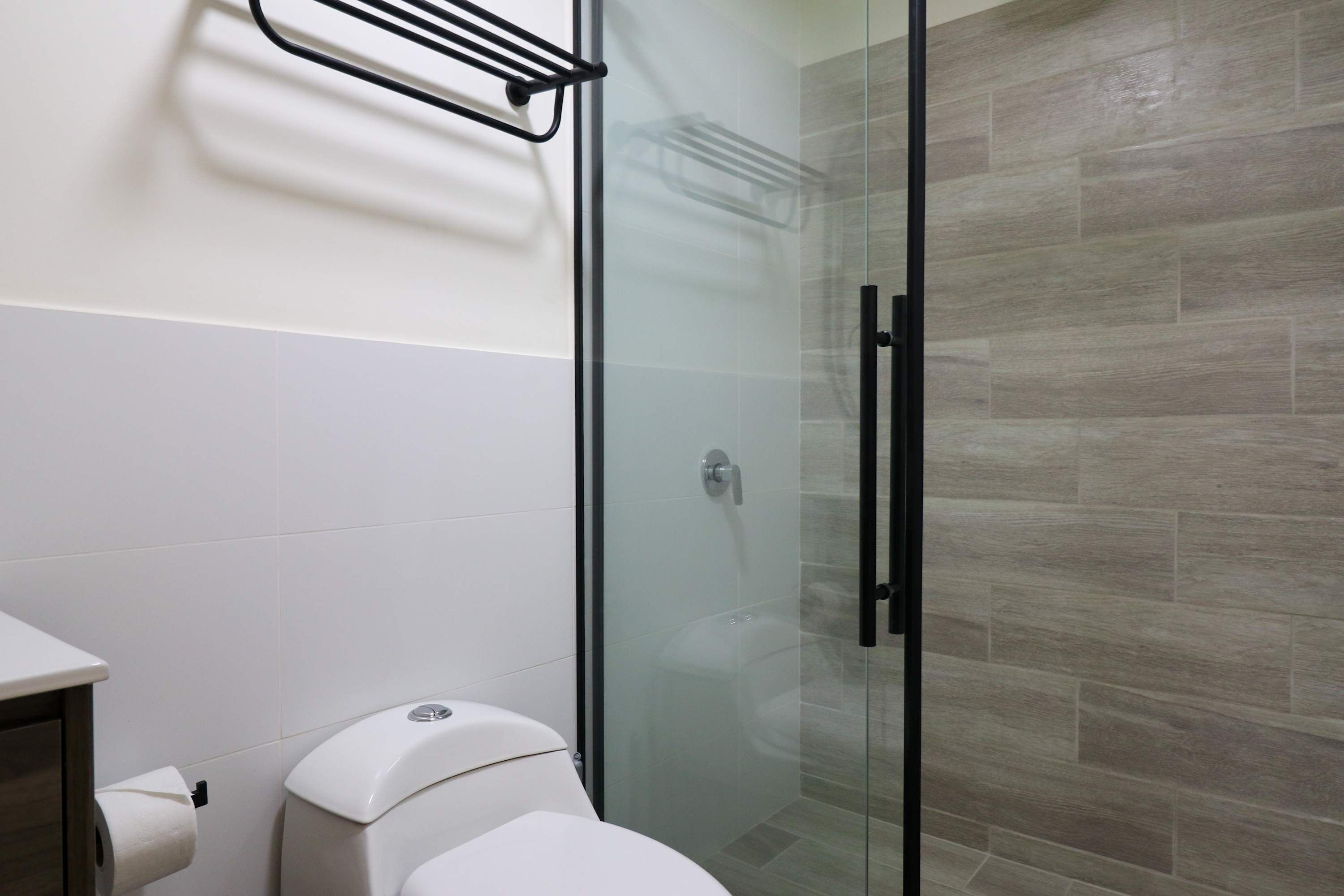 A bathroom with a glass shower enclosure, a toilet, and a towel rack.