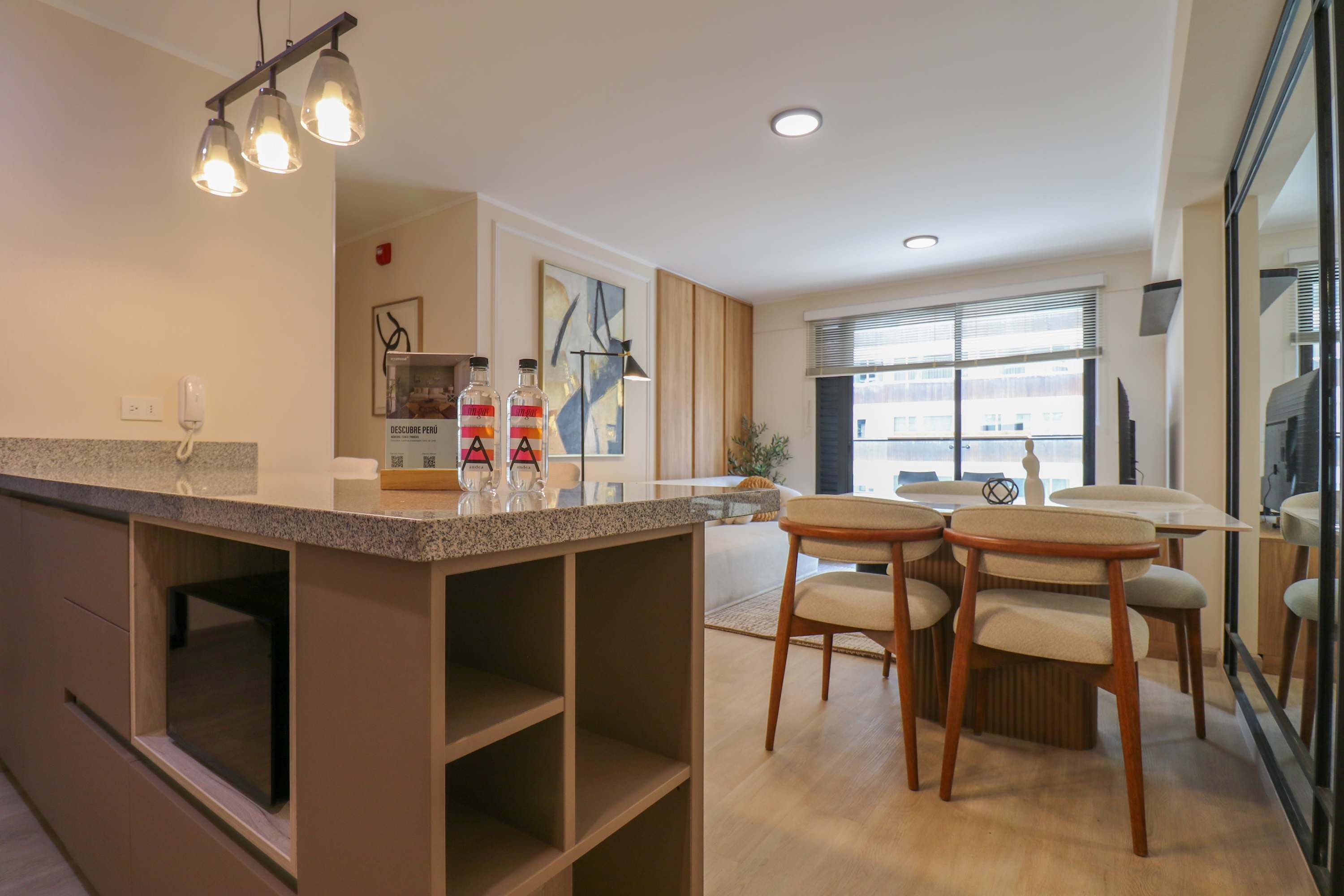 A modern kitchen with a granite countertop, wooden chairs, and pendant lighting.