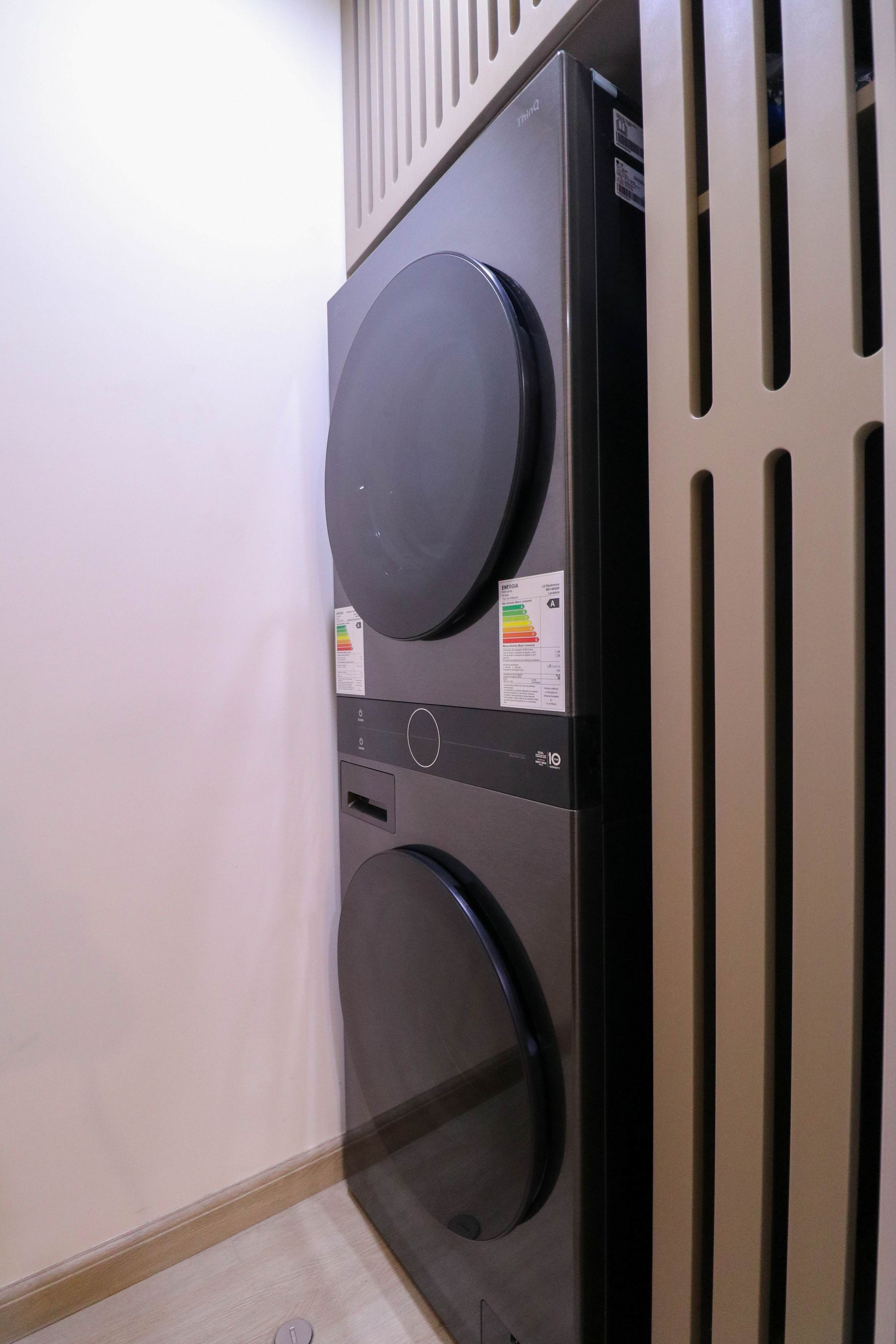 A compact, modern laundry room with two large, black appliances, a control panel, and a vented wall.