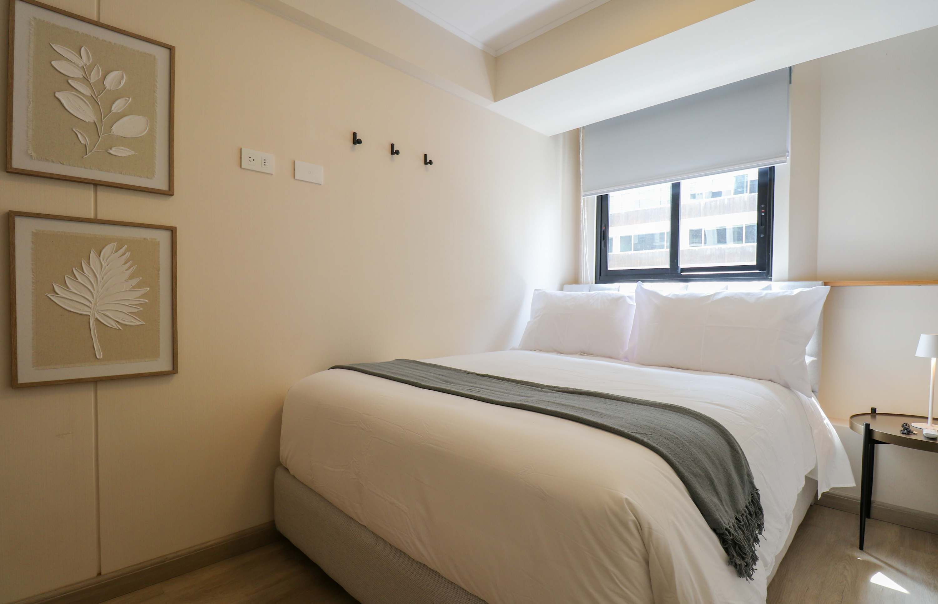 A bedroom with a bed, a nightstand, a lamp, and two framed leaf artworks on the wall.