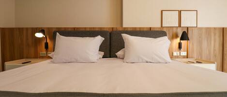 A double bed with white linens, two bedside tables with lamps, a wooden headboard, and a wall-mounted artwork.