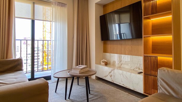 A modern living room with a sofa, a round table with books, a TV mounted on the wall, and a balcony with curtains. - w Luxury 3BR w Balcony in Upscale Miraflores (Lima)