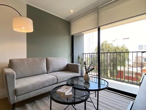 Ein modernes Wohnzimmer mit einer Couch, einem Glastisch und Blick auf die Stadt durch große Fenster.