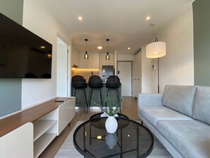 A modern living room with a sofa, a coffee table with a vase, and a TV mounted on the wall. - w Deluxe 2BR w Balcony View in Miraflores (Lima)