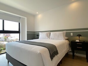A modern bedroom with a large bed, a nightstand, a lamp, and a view of the outside. - w Deluxe 2BR w Balcony View in Miraflores (Lima)