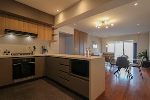 A modern kitchen with built-in appliances, a dining area with a glass table, and a view of the outdoors. - w Homey 3BR With Balcony in Miraflores (Lima)