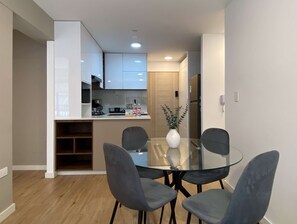 Eine moderne Küche mit weißen Schränken, einem Glastisch und vier grauen Stühlen.