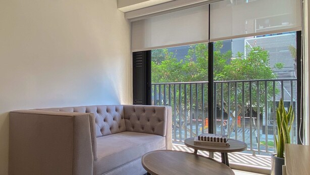 Ein modernes Zimmer mit grauem Sofa, einem kleinen runden Tisch und Blick durch große Fenster nach draußen.
