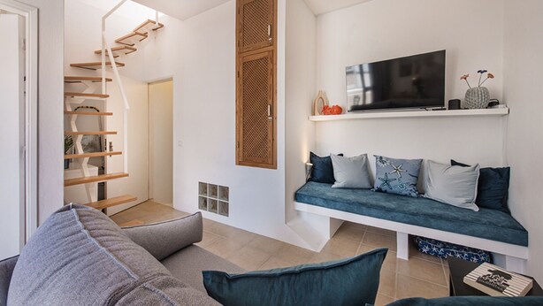 A modern living room with a staircase, a sofa, a TV, and a shelf with decorative items. - Casa M.V. Slater - CharmingTavira Townhouse with Rooftop Terrace (Pet friendly) (Tavira)