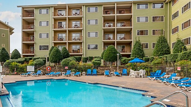Una piscina con lettini da sole e un palazzo a più piani sullo sfondo.