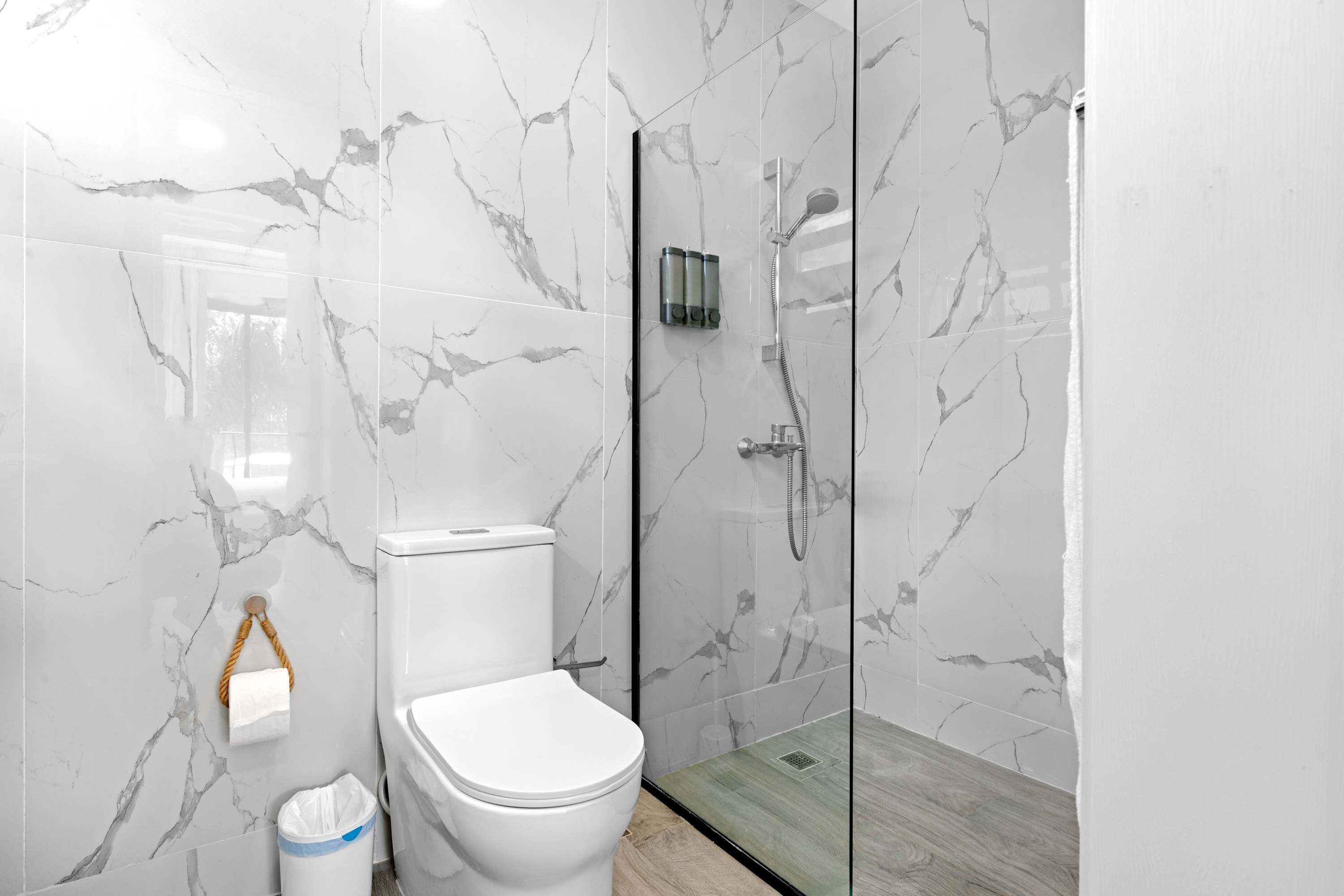 Un baño con inodoro, cabina de ducha de vidrio y paredes con diseño de mármol.