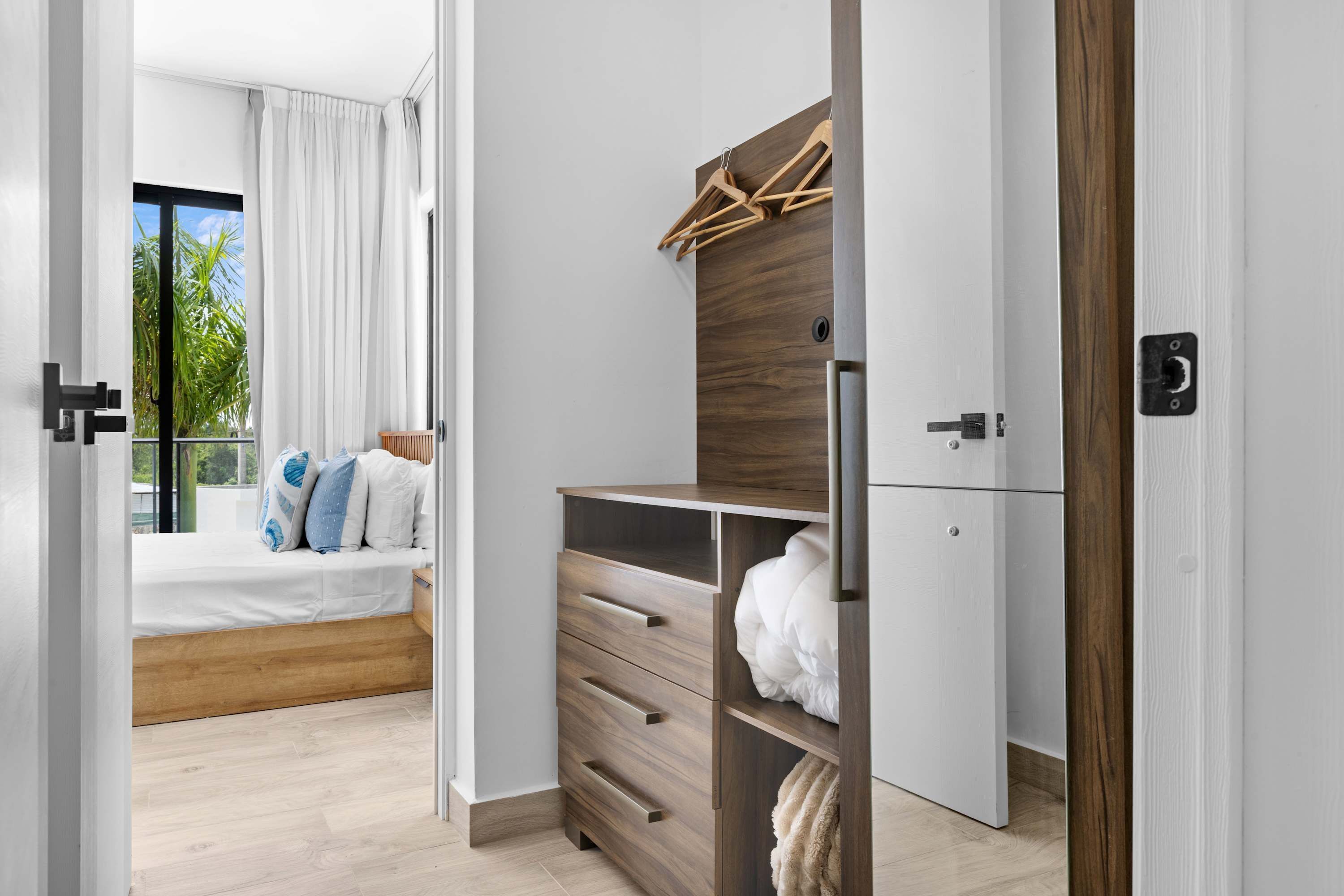 Une chambre à coucher moderne avec un lit, une armoire en bois, un portant et une vue sur l’extérieur.