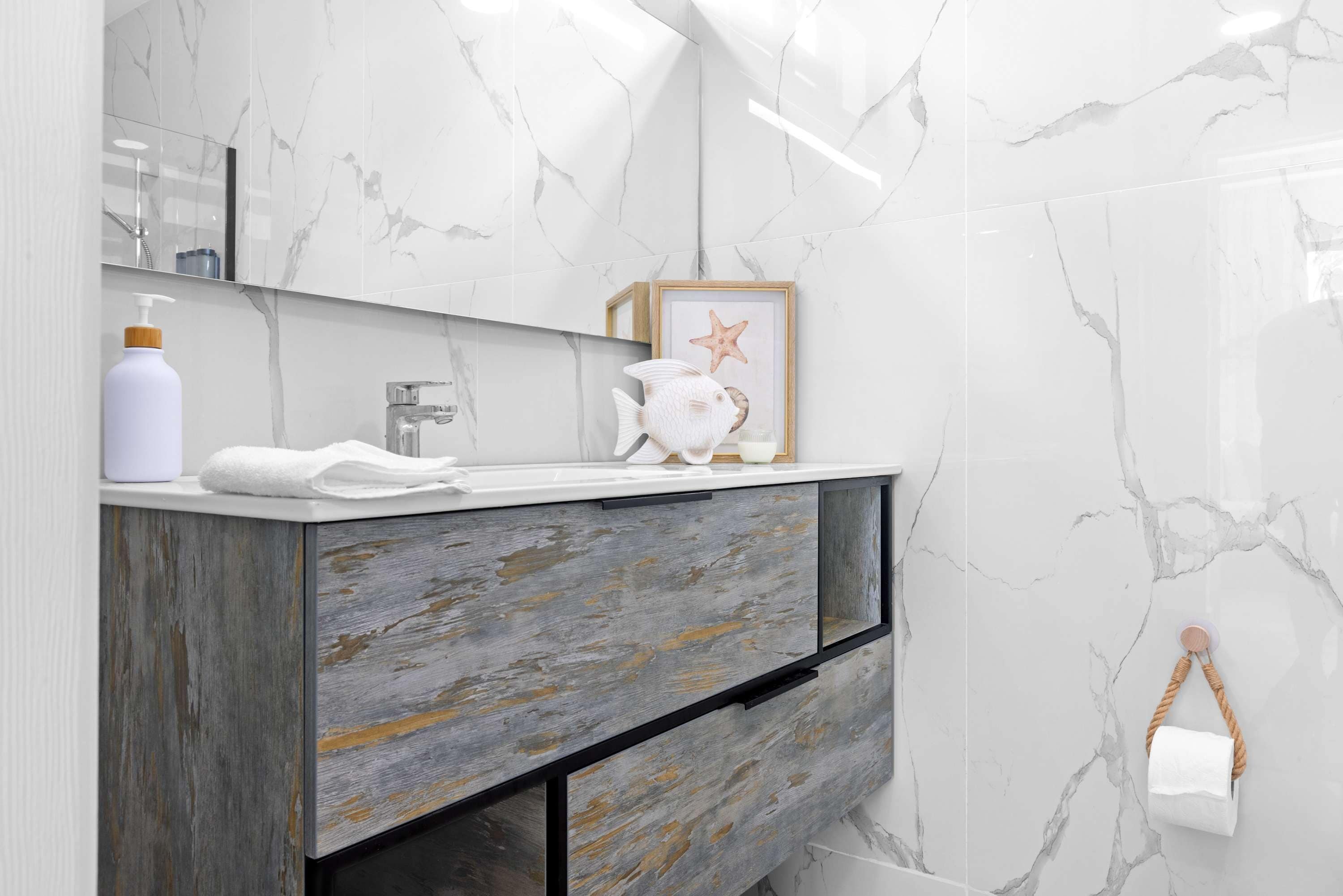 A bathroom with a marble wall, a wooden vanity, a framed starfish decoration, and a towel hanging on a hook.