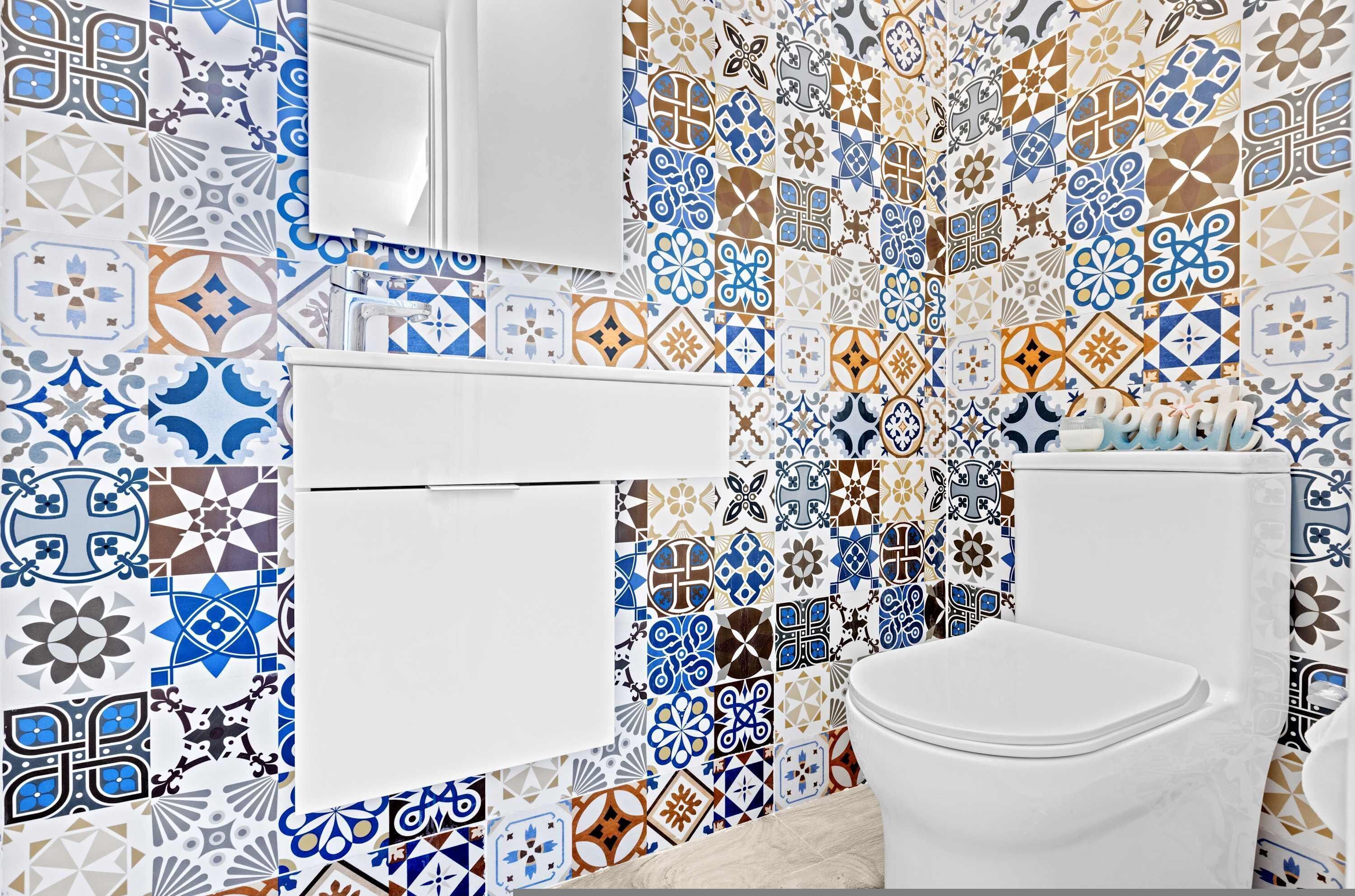 A bathroom with a white toilet, a sink, and a mirror. The walls are covered with a variety of geometric and floral tile patterns.