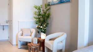 Un salon moderne avec un fauteuil blanc, une petite table en bois, un lampadaire et un tableau représentant des voiliers accroché au mur.