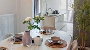 Un coin repas avec une table blanche dressée pour quatre personnes, comprenant des assiettes, des bols et des couverts.