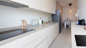 Una cucina moderna con mobili bianchi, un piano di lavoro nero, un piano cottura integrato e un'area pranzo con tavolo e sedie.
