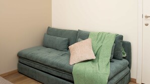 Un divano verde con una coperta verde e un cuscino beige in una stanza con una porta bianca.