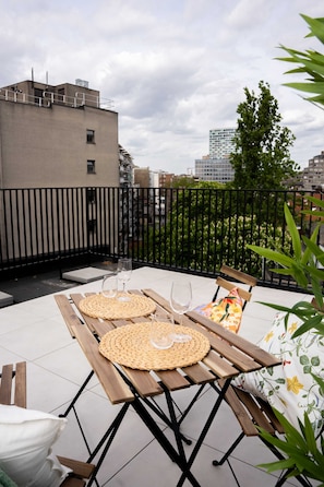 Eine Dachterrasse mit Holztisch, gedeckt für zwei Personen, zwei Weingläser und einer gewebten Tischmatte.