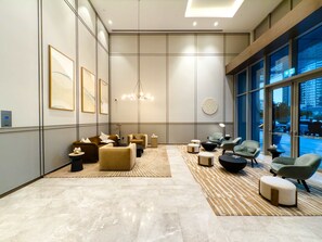 A modern lobby with a marble floor, sofas, armchairs, a chandelier, artwork, and large windows with a city view. - One Lux Stay Grande Signature Residence 2BR - Direct Burj Khalifa View (Dubai)