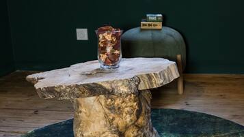 Een rustieke houten tafel met een glazen vaas op een groene vloerkleed, een raam met uitzicht, en een doosje met de tekst 'Pixies' op de achtergrond.