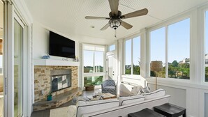 Ein sonnendurchfluteter Raum mit Kamin, Fernseher, Sofa und Deckenventilator.