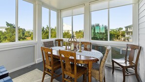 Ein Wintergarten mit großem Tisch und Stühlen, großen Fenstern und Blick ins Grüne.