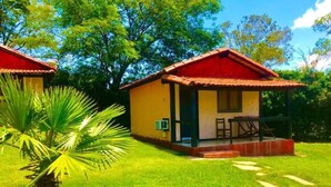 A small, single-story building with a red roof, a porch with a table and chairs, and a well-maintained lawn. - Pousada Village Da Serra (Santana do Riacho)
