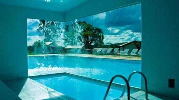 A swimming pool with a waterfall view, clear water, and a poolside area with lounge chairs. - Pousada Village Da Serra (Santana do Riacho)