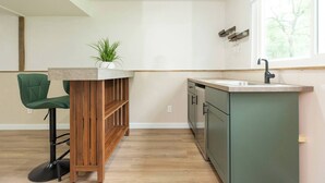 Een moderne keuken met een houten barstoel, een groene stoel, een ingebouwd spoelgedeelte en een raam met uitzicht op bomen.