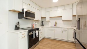 Een moderne keuken met witte kastjes, een zwarte kookplaat en een roestvrijstalen koelkast.
