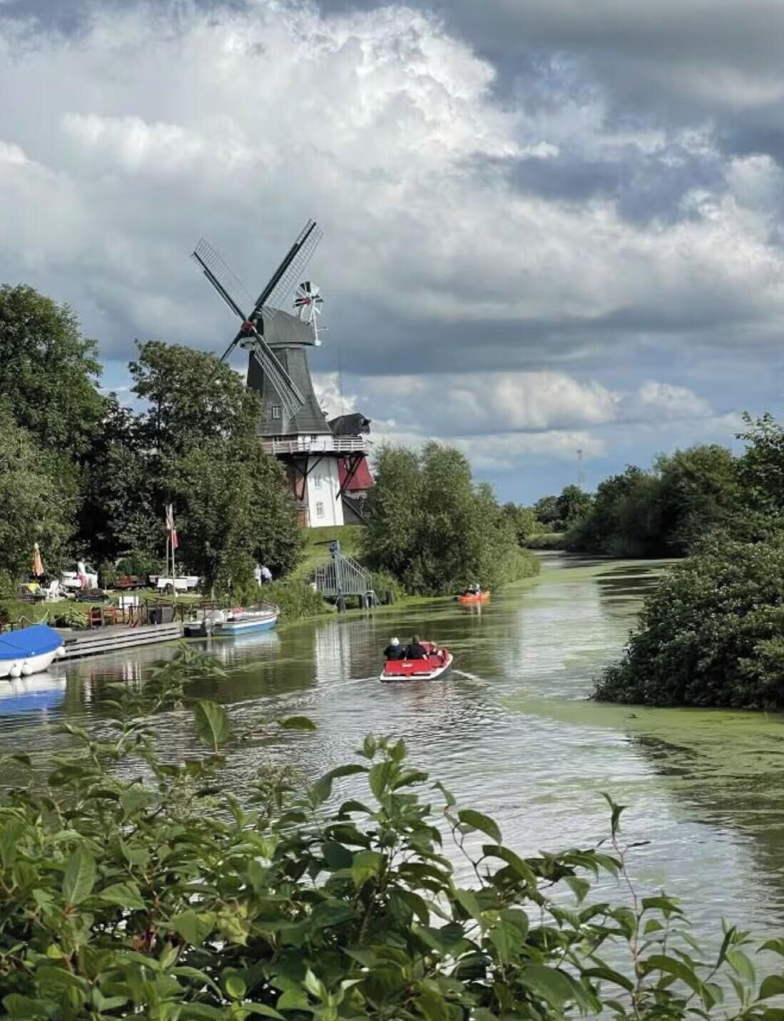 A river with boats, a windmill, and greenery.