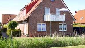 Ein zweistöckiges Backsteinhhaus mit rotem Dach, einem Balkon mit weißen Geländern und einem kleinen Garten.