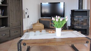Ein Wohnzimmer mit Fernseher, Kamin, einer Holzkommode und einem Tisch mit Gläsern und Tulpen.