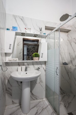A bathroom with a white sink, marble walls, a glass shower enclosure, and a small potted plant. - Art House Near to Saint George Beach by Konnect (Corfu)