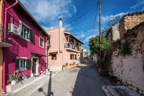A narrow street with buildings on either side, some with balconies and potted plants. - Art House Near to Saint George Beach by Konnect (Corfu)