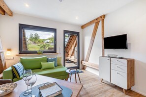 Ein modernes Wohnzimmer mit einem grünen Sofa, einem Esstisch mit Schüssel und Weinglas, einem Fernseher an der Wand und Blick auf eine Holztreppe.