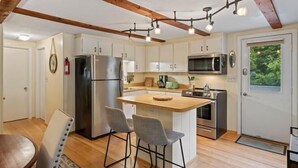 A modern kitchen with white cabinets, a stainless steel refrigerator, a microwave, and a built-in oven. There is a small island with bar stools. - Lovely home walking distance to community beach sleeps 6 (Moultonborough)
