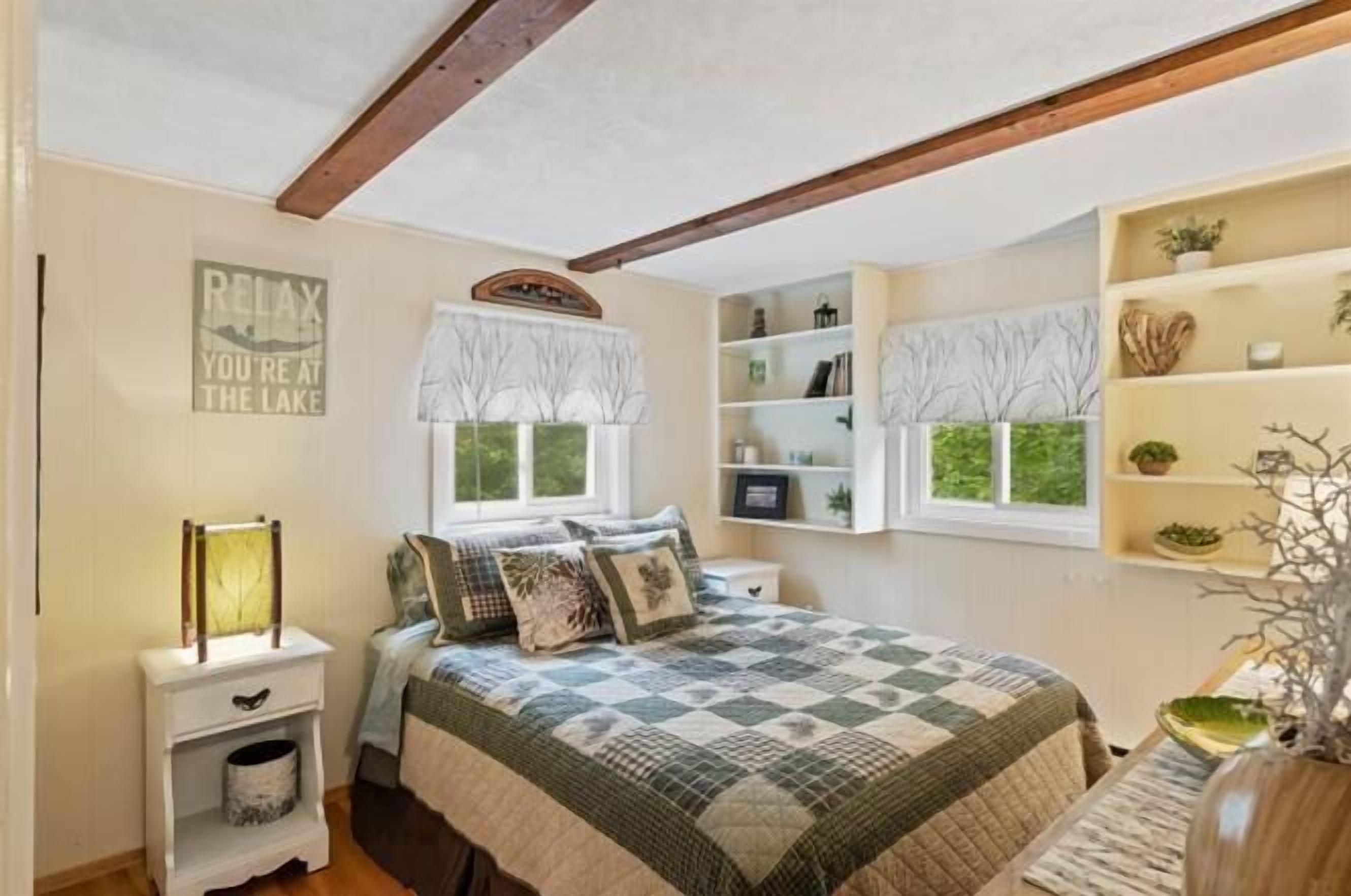 Une chambre à coucher avec un lit, une table de chevet, une étagère avec des plantes et une fenêtre donnant sur des arbres.