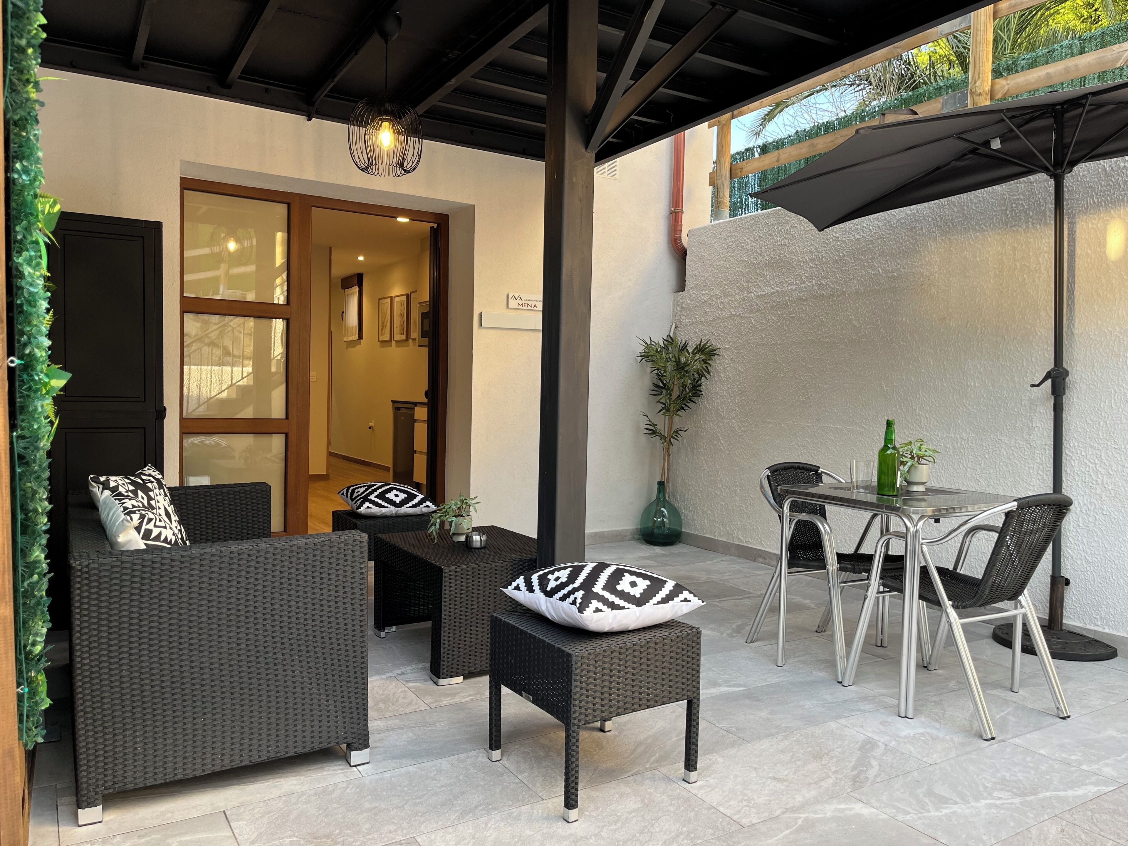 An outdoor patio area with wicker furniture, a table, chairs, and a potted plant.