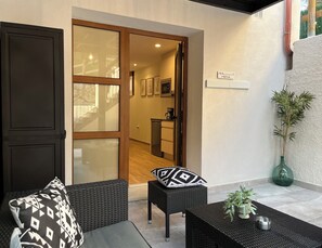 A modern outdoor seating area with wicker furniture, a small table with a plant, and a door leading to a kitchen area. - Apartment in the Picos de Europa, Asturias. (Onis)