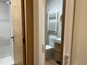 Une porte en bois donne accès à une salle de bain équipée de toilettes, d’un lavabo et d’un porte-serviettes.