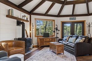 A cozy living room with a fireplace, leather sofa, and a large window offering a view of the outdoors. - Charming Modern‑Rustic Retreat with a Chef’s Kitchen (Blanchard)