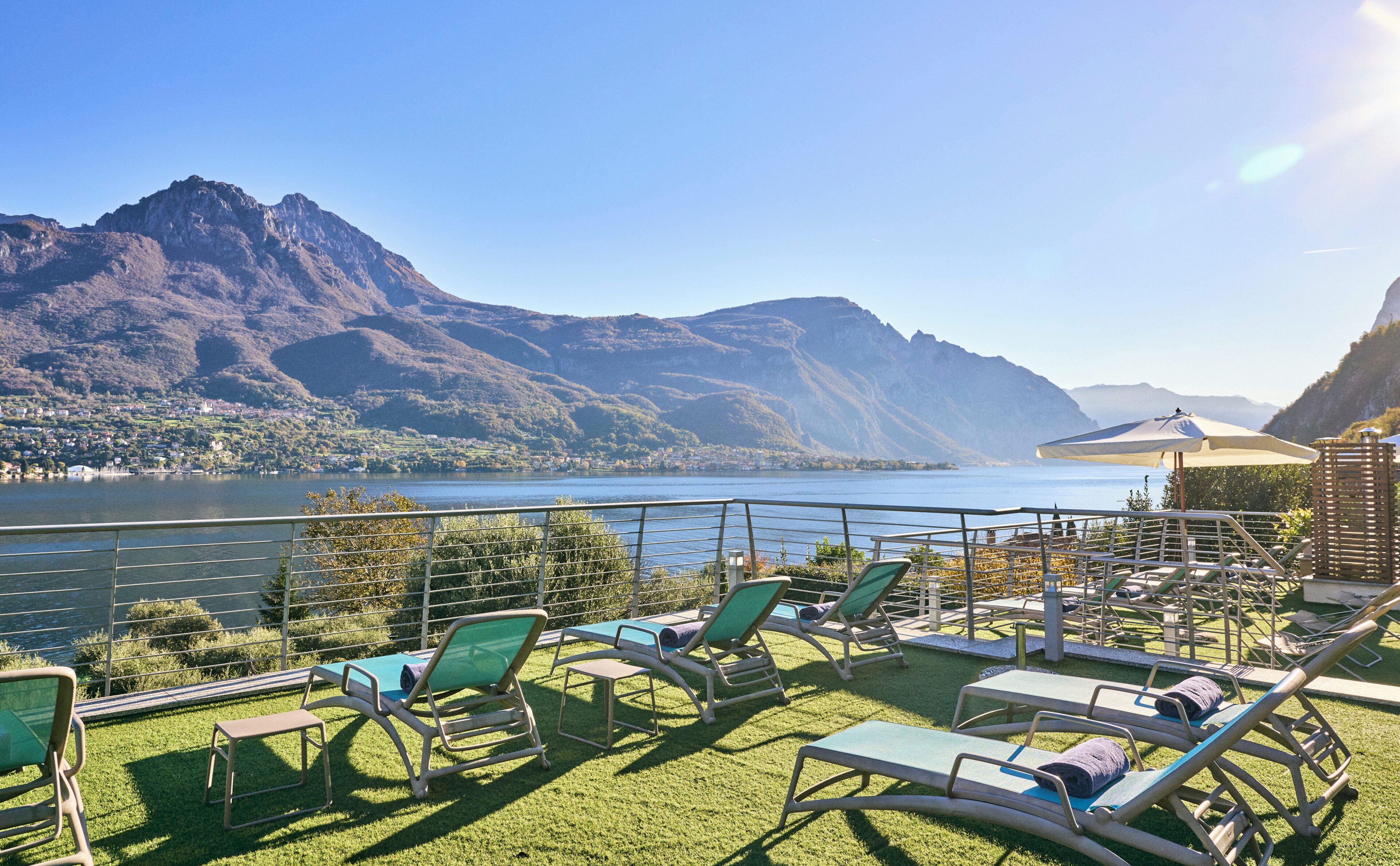 A terrace with lounge chairs overlooking a lake and mountains.