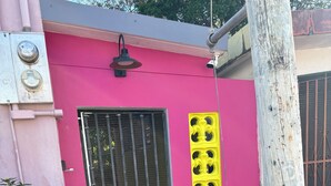 A pink building with a barred gate, a yellow decorative panel, and a brick planter with green foliage. - Perfect Studio in the heart of Isabel! Walkable to all the bars and restaurants (Vieques)