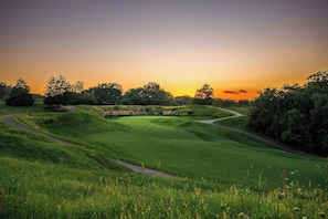 A golf course with rolling hills, a winding path, and a sunset in the background. - Farmstead Tee & Ski - Resort Core location, Fireplaces, Dog Friendly (Galena)