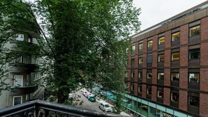 Un edificio de varios pisos con fachada de ladrillo, un balcón con barandilla de metal decorativa y una calle con coches estacionados abajo.